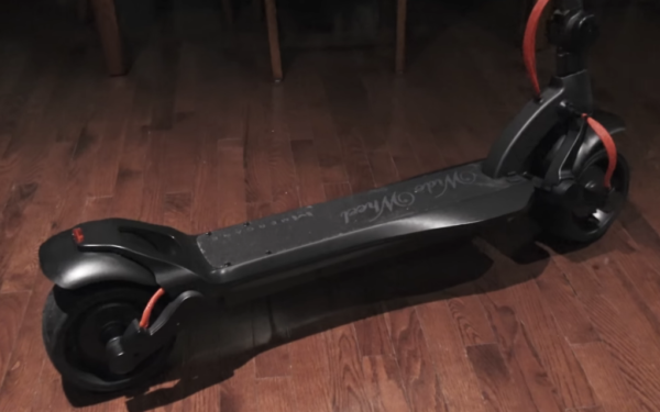 rear diagonal view of a black Mercane Widewheel Single electric scooter with red details in a living room
