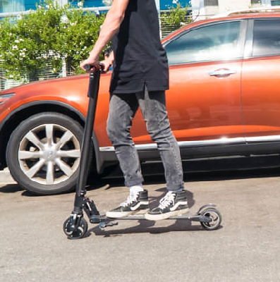 person riding a black Swagtron Swagger with an orange car in the background