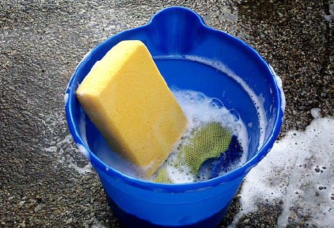 a big yellow sponge in a blue bucket half filled with soap water
