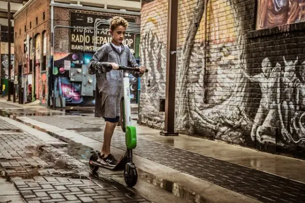 boy riding a white Lime electric scooter on a wet street in a city