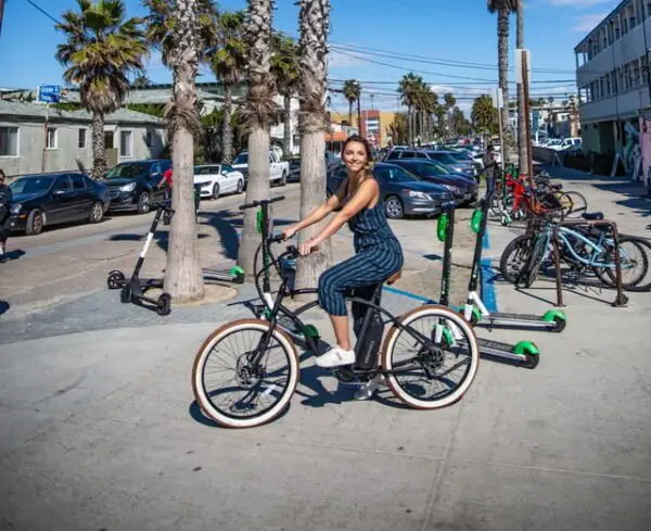 girl waiting on an electric bike with several Lime and Bird rental electric scooters in the background