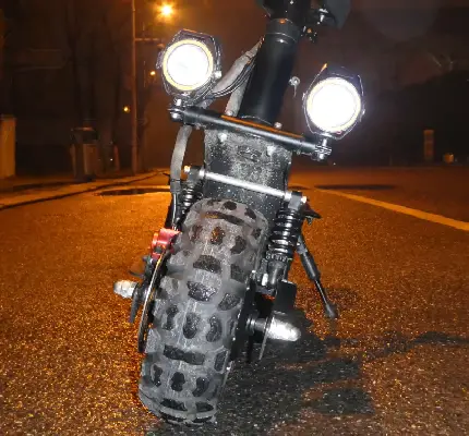 lower front part of electric scooter with two round headlights turned on and shining in the night