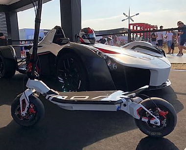 white Rion2 RE90 electric scooter with black details standing next to a racing car