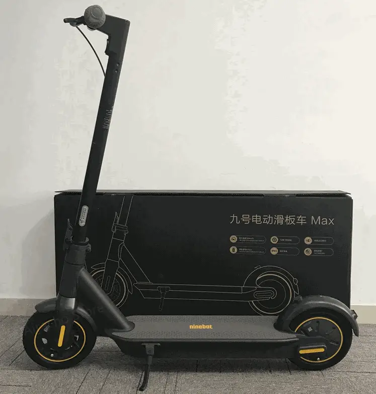 side view of a black Ninebot Max with yellow details standing next to its box