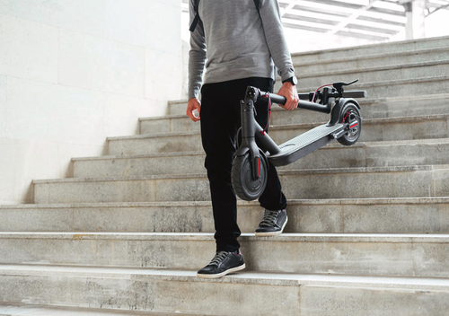 A guy carrying a folded e-scooter down steps
