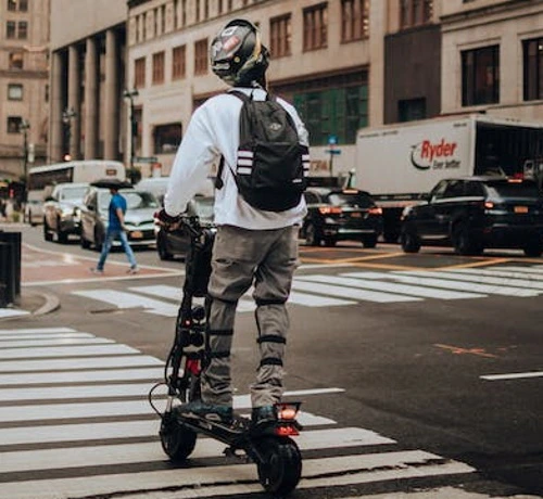 A man crossing a road on an electric scooter wearing a helmet and knee pads