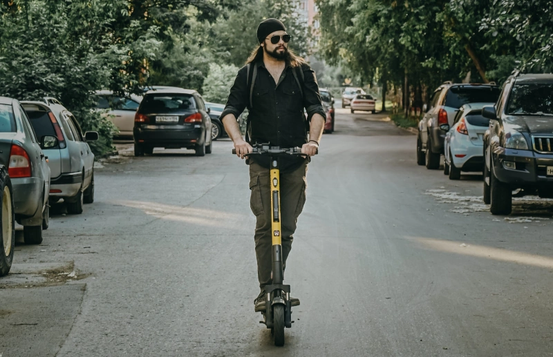 A man riding his electric scooter with parked cars on both sides