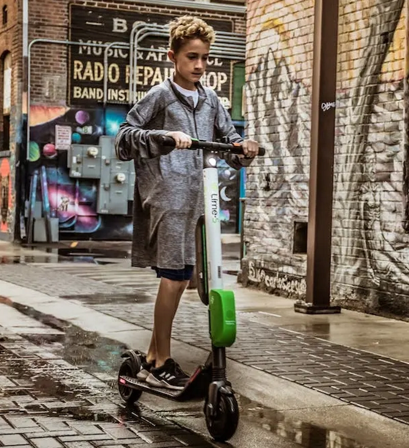 A teenager riding an electric scooter on rain