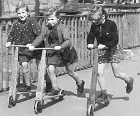black and white photo of 3 children riding kick scooters