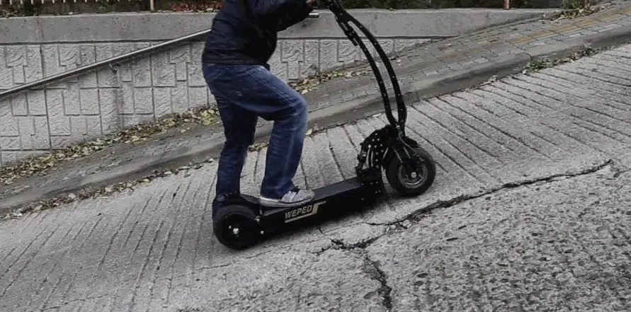 person climbing a hill on an electric scooter, leaning forward