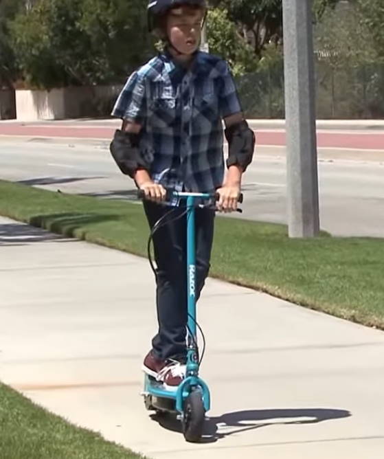 a kid riding a Razor E200 on a sidewalk