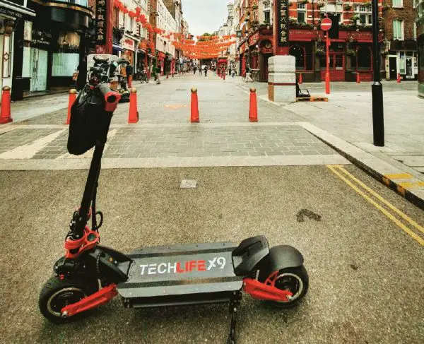 side view of the Techlife X9 electric scooter leaning on its stand in a city street