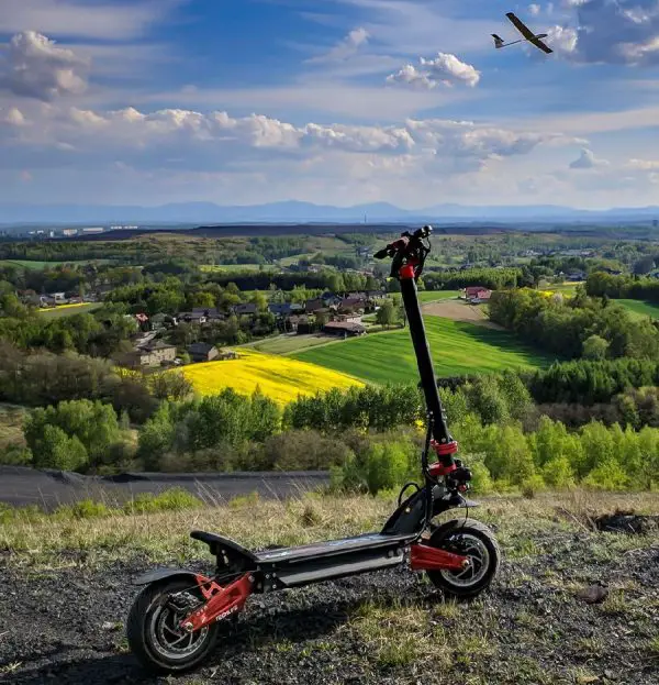 Techlife X9 electric scooter climbed on a hill overlooking green fields and blue skies